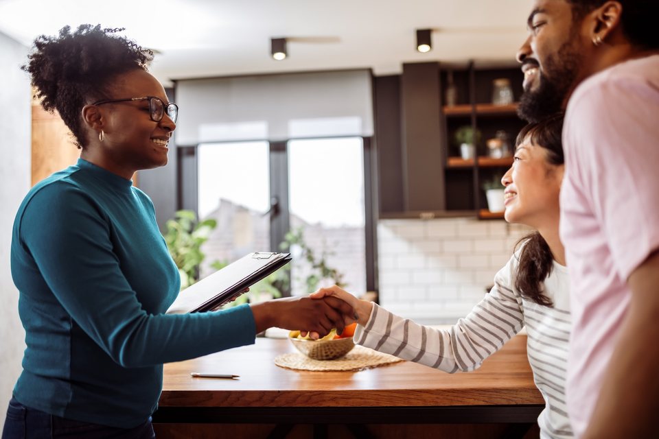 A landlord with a clipboard shaking hands with her new tenants in the kitchen of a rental
